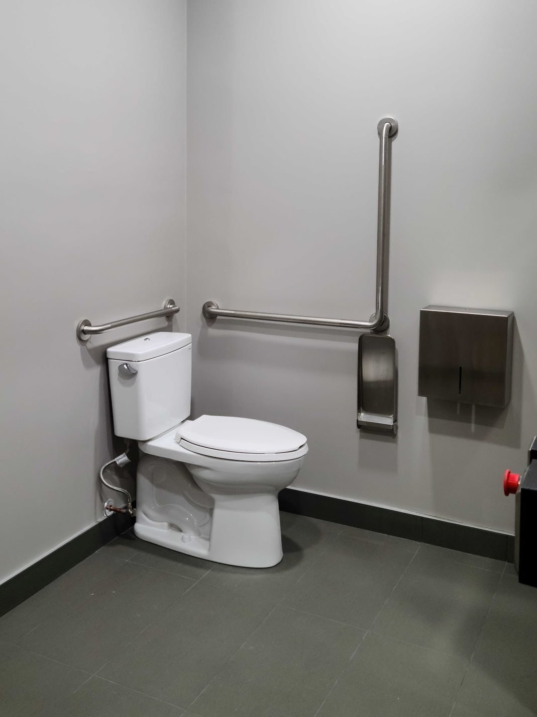 Restroom toilet with large adjacent space, horizontal and vertical grab bars, toilet paper dispenser, and collapsible wall shelf