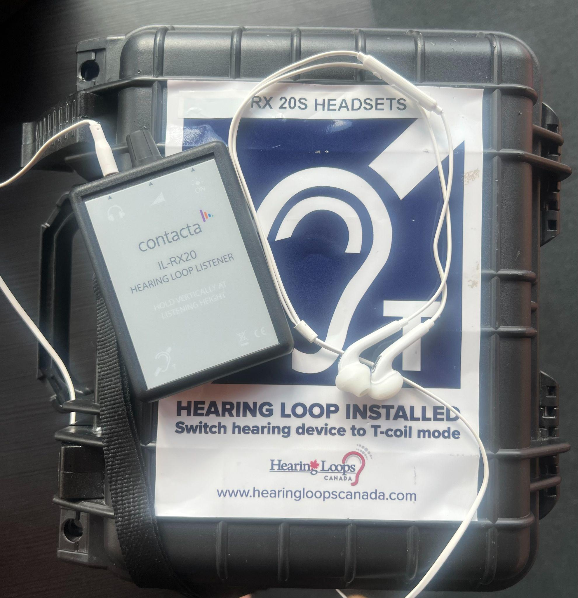 A Shoctor T-Coil Hearing Loop headset which includes earbuds placed on top of the Hearing Loop box.