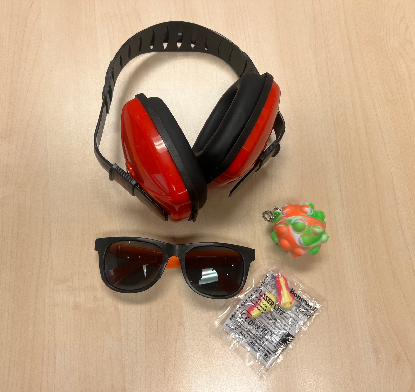 The items found in a Citadel Theatre Sensory kit are displayed. These items include a set of soft earplugs, a fidget item, adjustable ear muffling headphones, and sunglasses.
