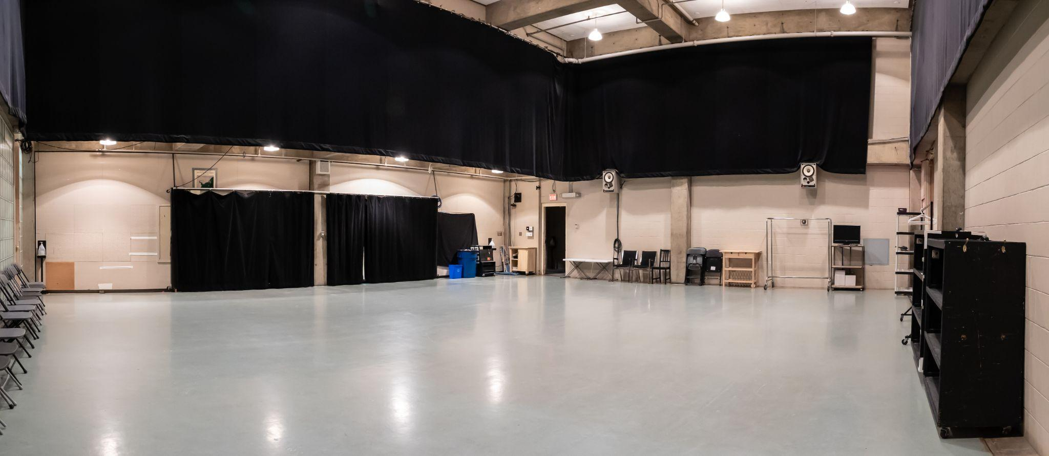 View of Shoctor Rehearsal Hall from a corner. There are mirrors covered by curtains and a sprung, open flooring space.